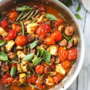 A large sauté pan with baked cherry tomatoes, feta, sausage, and green beans.