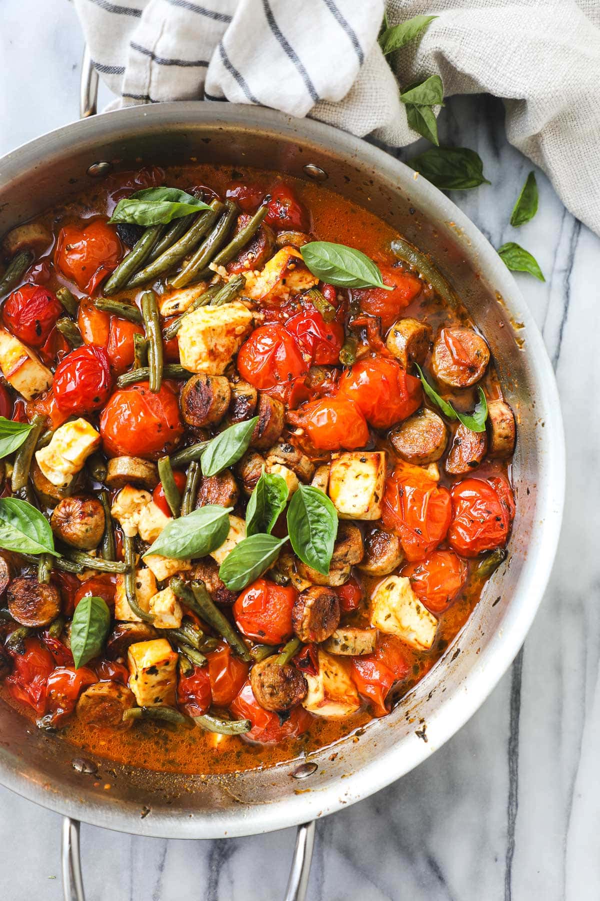 A large sauté pan with baked cherry tomatoes, feta, sausage, and green beans.