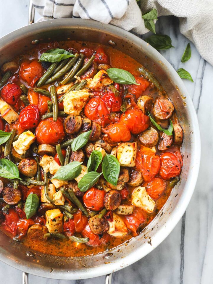 A large sauté pan with baked cherry tomatoes, feta, sausage, and green beans.
