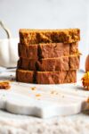 Four slices of pumpkin bread stacked on top of each other on a marble serving board.