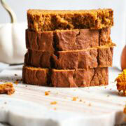 Four slices of pumpkin bread stacked on top of each other on a marble serving board.