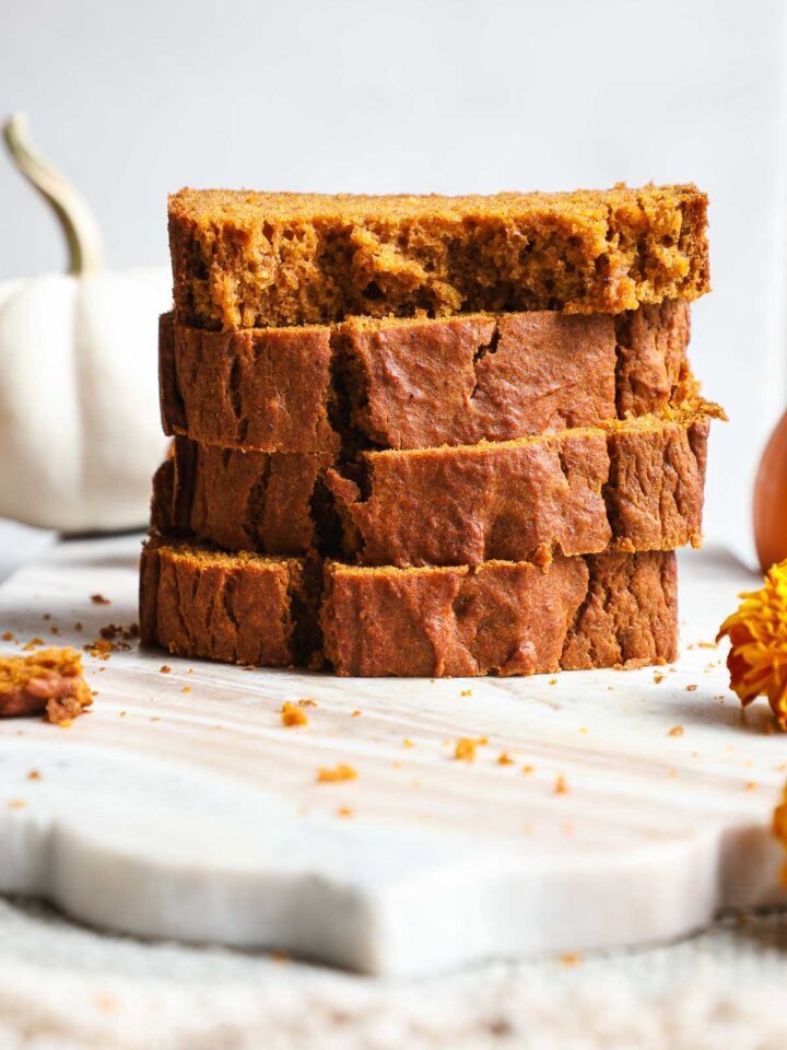 Four slices of pumpkin bread stacked on top of each other on a marble serving board.