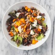 Butternut Squash Salad with Maple Vinaigrette in a large white salad bowl including maple roasted butternut squash, farro, goat cheese, and toasted pecans.