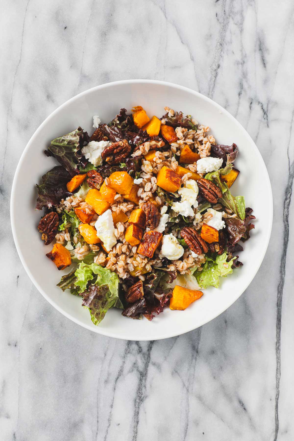 Butternut Squash Salad with Maple Vinaigrette in a large white salad bowl including maple roasted butternut squash, farro, goat cheese, and toasted pecans.
