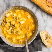 A bowl of vibrant orange Honeynut Squash Soup with Italian Sausage, cauliflower, and ditalini pasta.