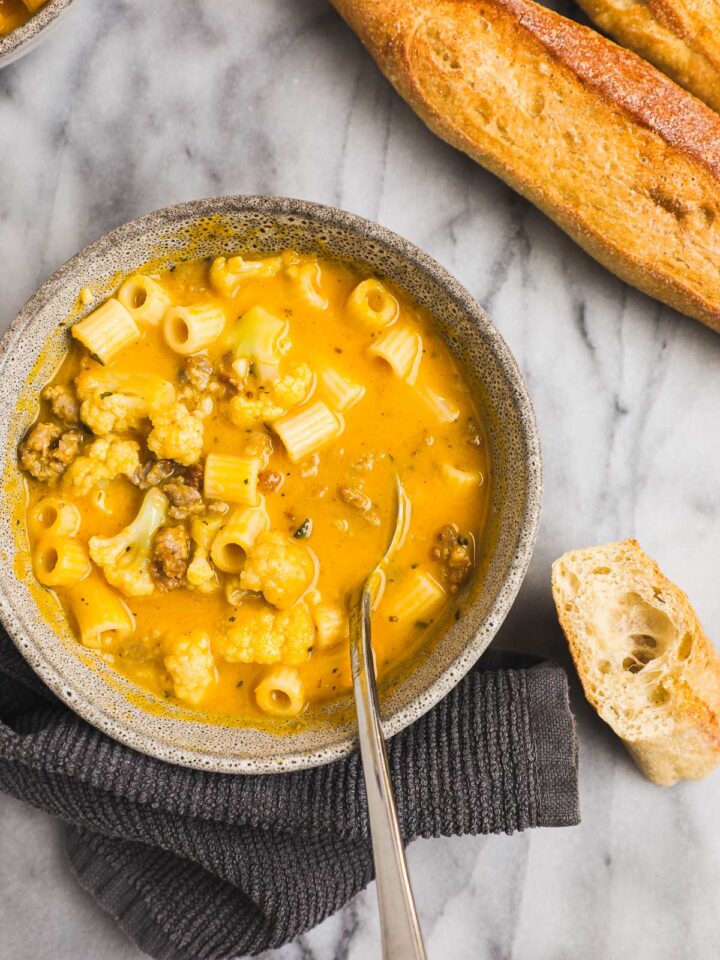 A bowl of vibrant orange Honeynut Squash Soup with Italian Sausage, cauliflower, and ditalini pasta.