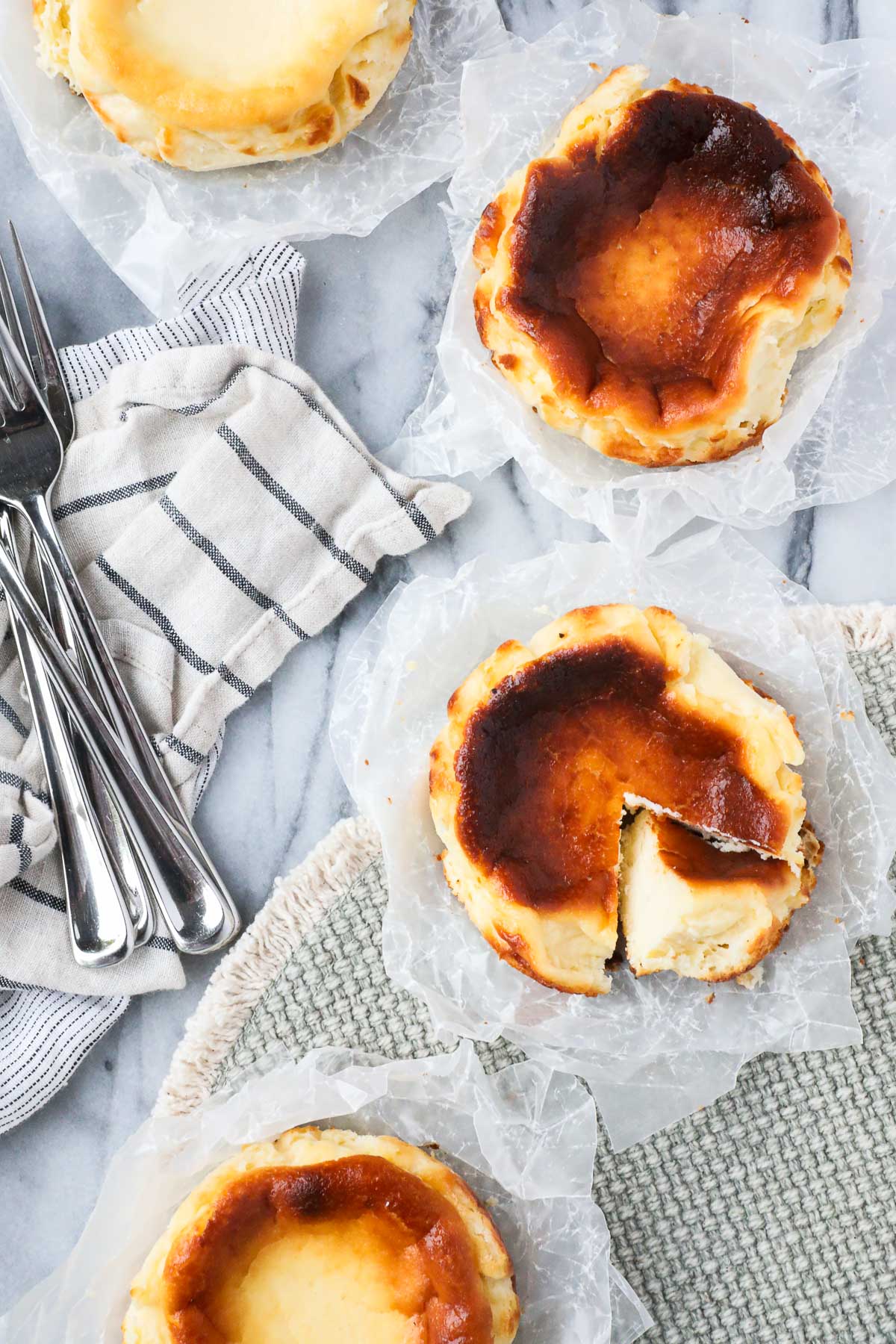 Four Mini Basque Cheesecakes arranged in a semi-circle with one of the cheesecakes with a slice cut out and turned on its side to show the creamy interior of the cake.