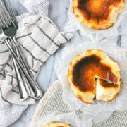 Four Mini Basque Cheesecakes arranged in a semi-circle with one of the cheesecakes with a slice cut out and turned on its side to show the creamy interior of the cake.