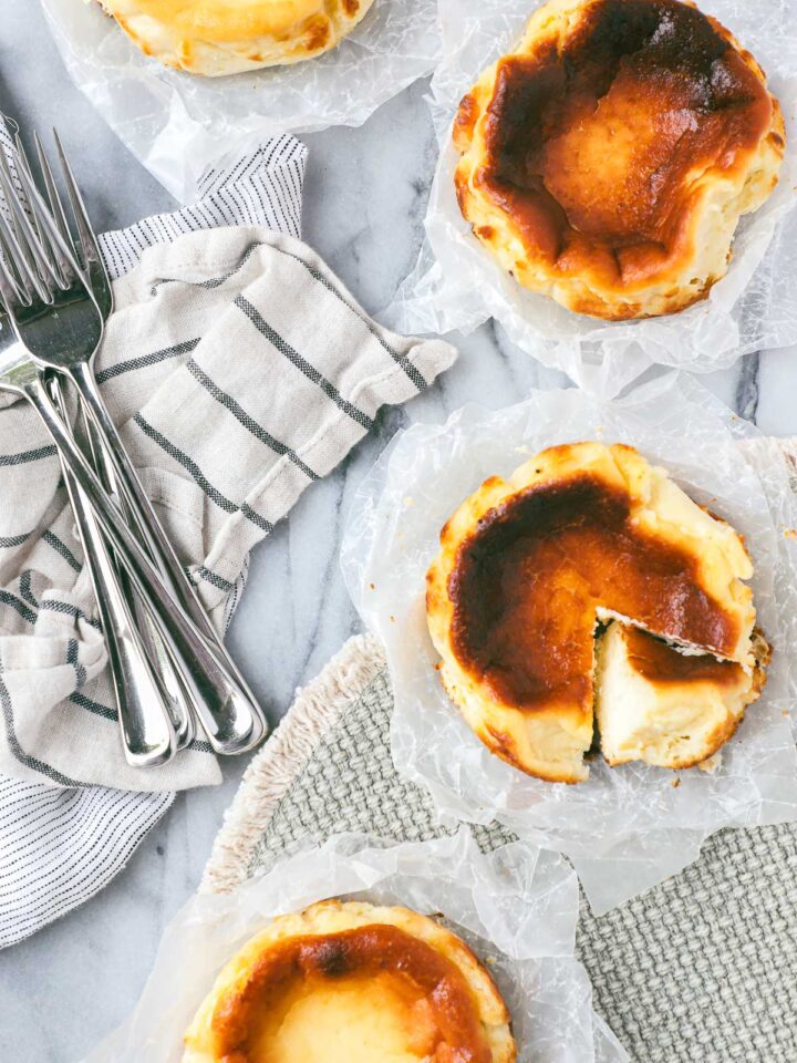 Four Mini Basque Cheesecakes arranged in a semi-circle with one of the cheesecakes with a slice cut out and turned on its side to show the creamy interior of the cake.