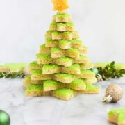 A Christmas Cookie Tree made with star shaped cut out sugar cookies decorated with green sanding sugar stacked on top of each other and topped with a cookie star decorated with yellow sugar.