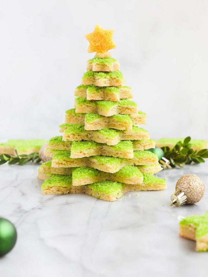 A Christmas Cookie Tree made with star shaped cut out sugar cookies decorated with green sanding sugar stacked on top of each other and topped with a cookie star decorated with yellow sugar.