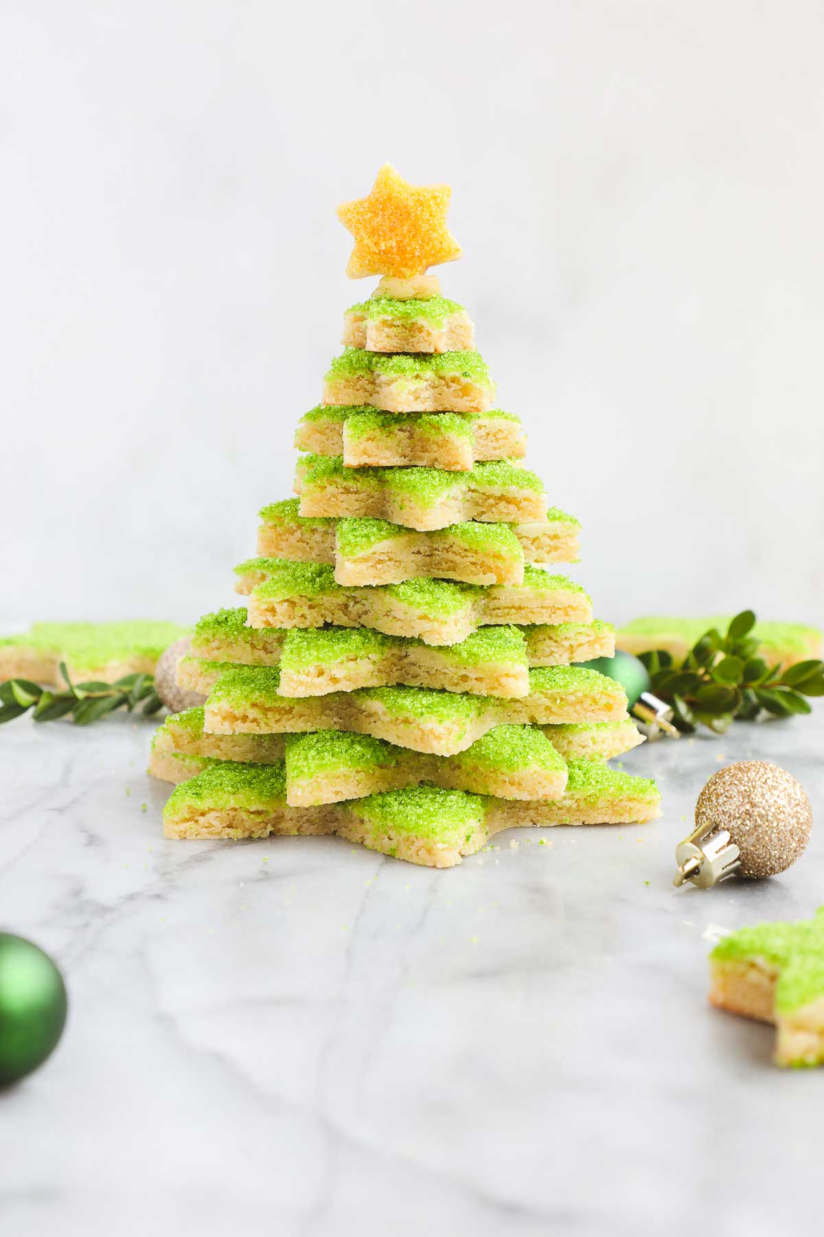 A Christmas Cookie Tree made with star shaped cut out sugar cookies decorated with green sanding sugar stacked on top of each other and topped with a cookie star decorated with yellow sugar.