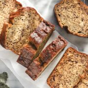 A loaf of Olive Oil Banana Bread cut into thick slices on a white backdrop.