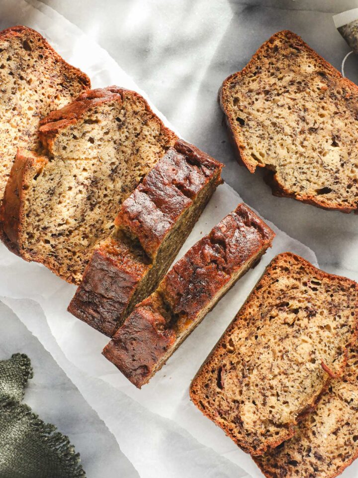 A loaf of Olive Oil Banana Bread cut into thick slices on a white backdrop.