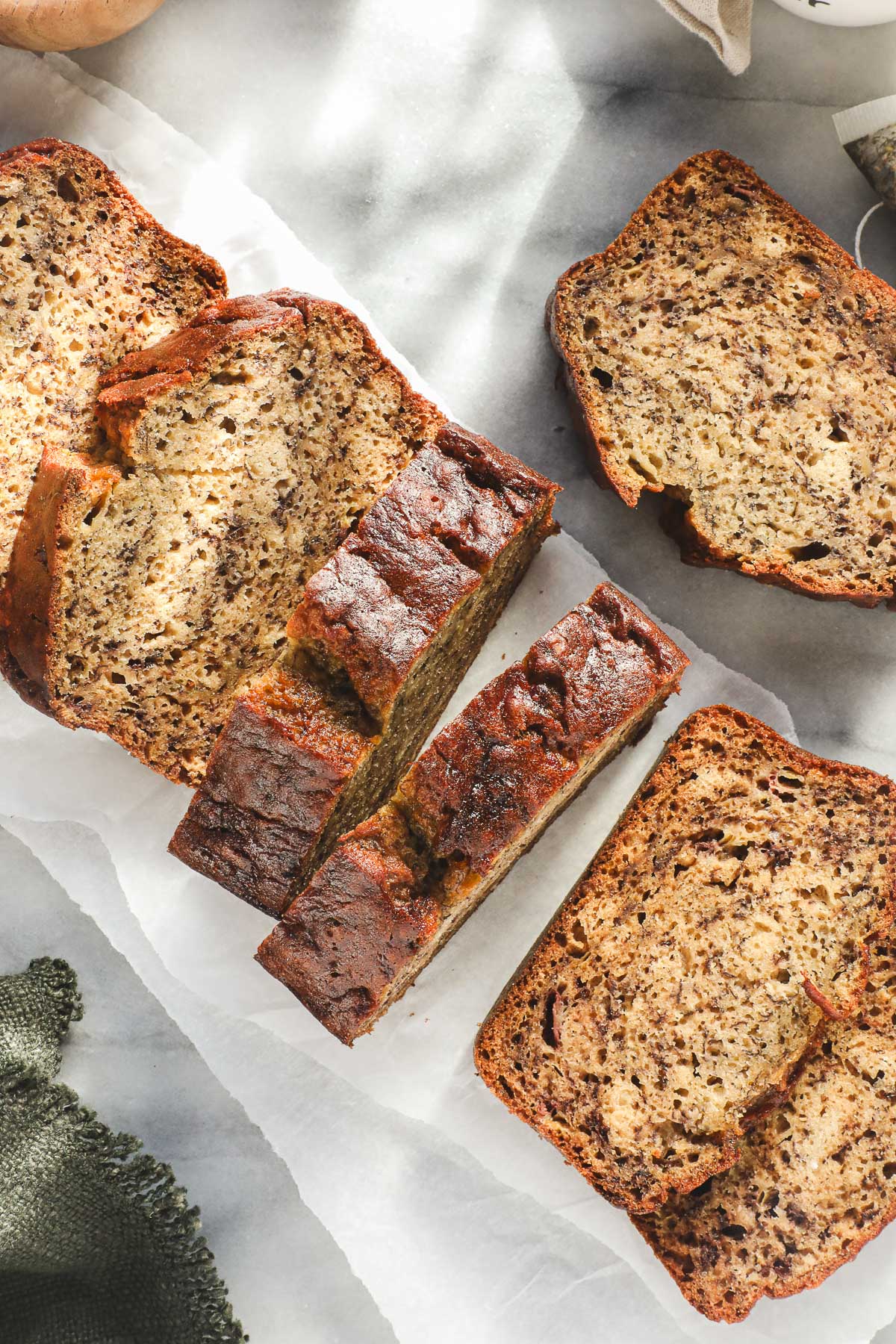 A loaf of Olive Oil Banana Bread cut into thick slices on a white backdrop.