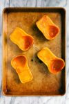 Two roasted honeynut squashes cut in half vertically and roasted on a gold baking sheet.