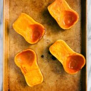 Two roasted honeynut squashes cut in half vertically and roasted on a gold baking sheet.