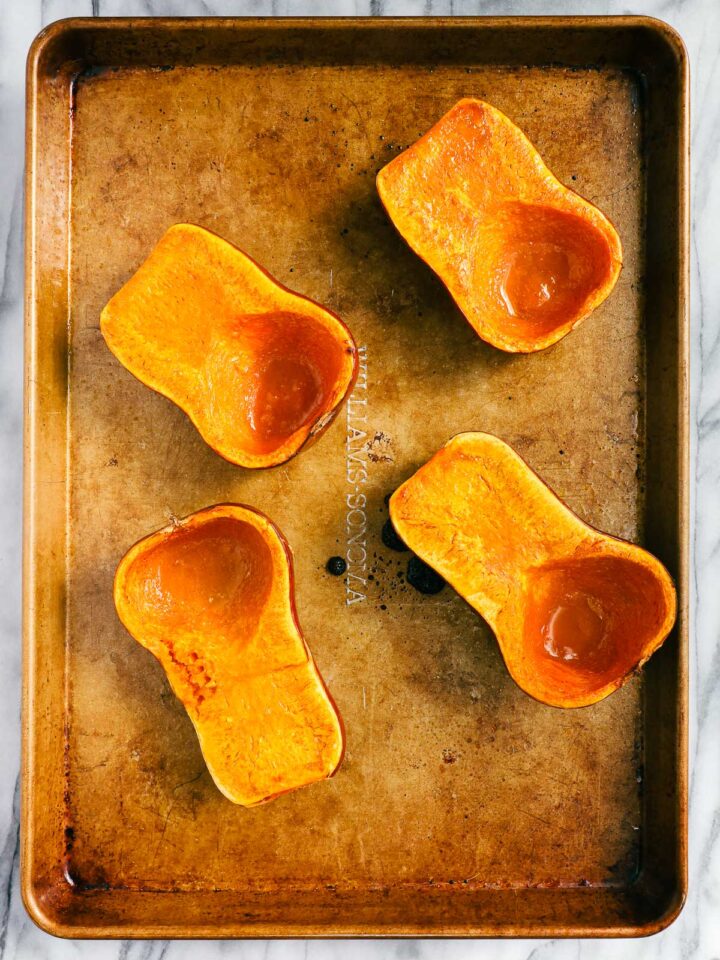Two roasted honeynut squashes cut in half vertically and roasted on a gold baking sheet.