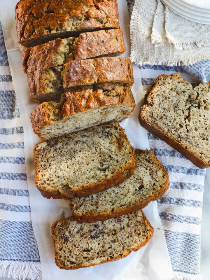 A loaf of Sourdough Banana Bread sliced on a light blue and white striped towel.