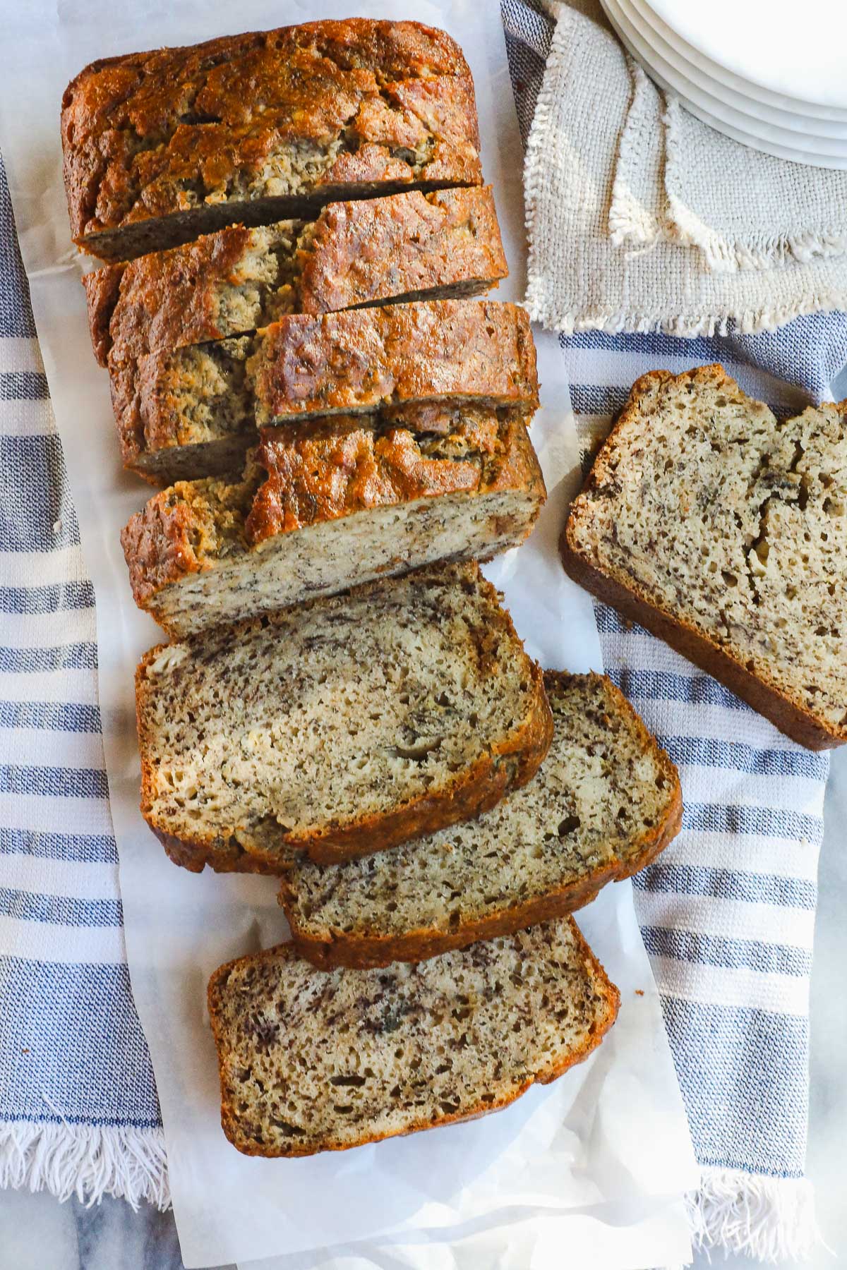 A loaf of Sourdough Banana Bread sliced on a light blue and white striped towel.