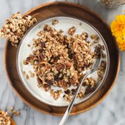 A bowl of yogurt topped with crunchy Sourdough Granola with yellow flowers and an orange yellow dish towel.