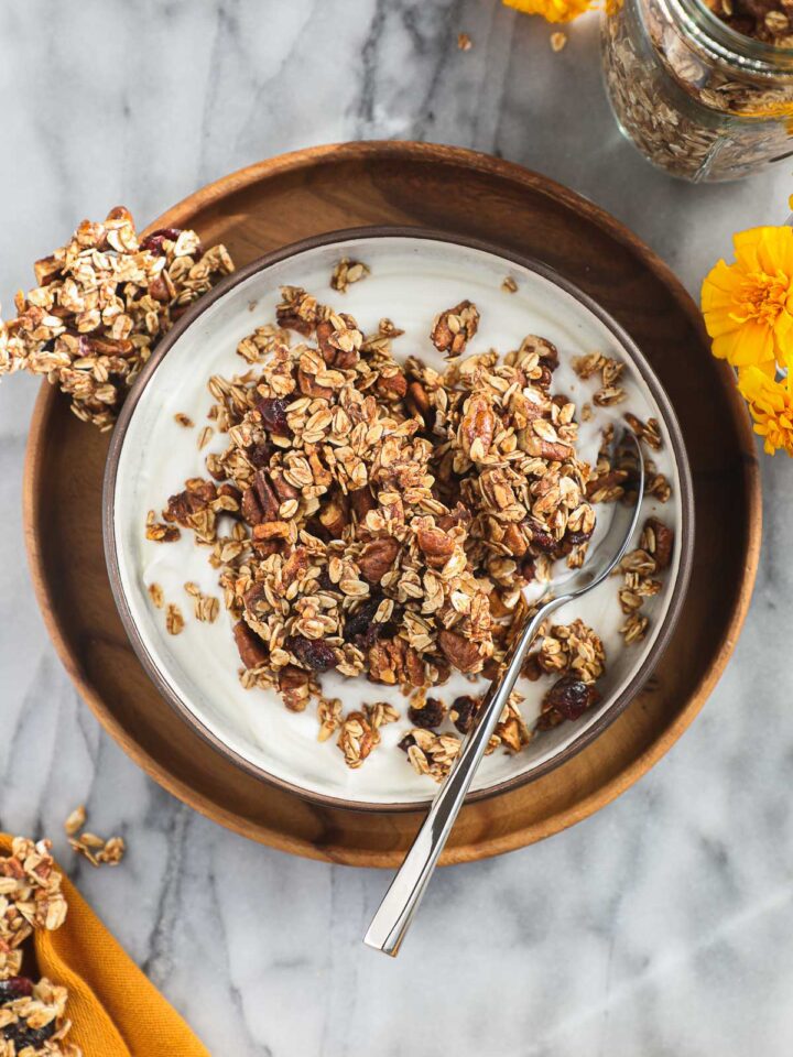 A bowl of yogurt topped with crunchy Sourdough Granola with yellow flowers and an orange yellow dish towel.