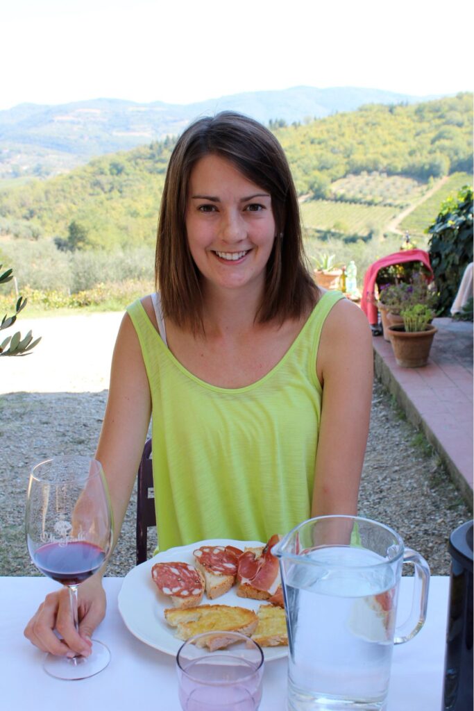 Lauren seated at a table with an appetizer and a glass of wine with the Tuscan hills in the background.