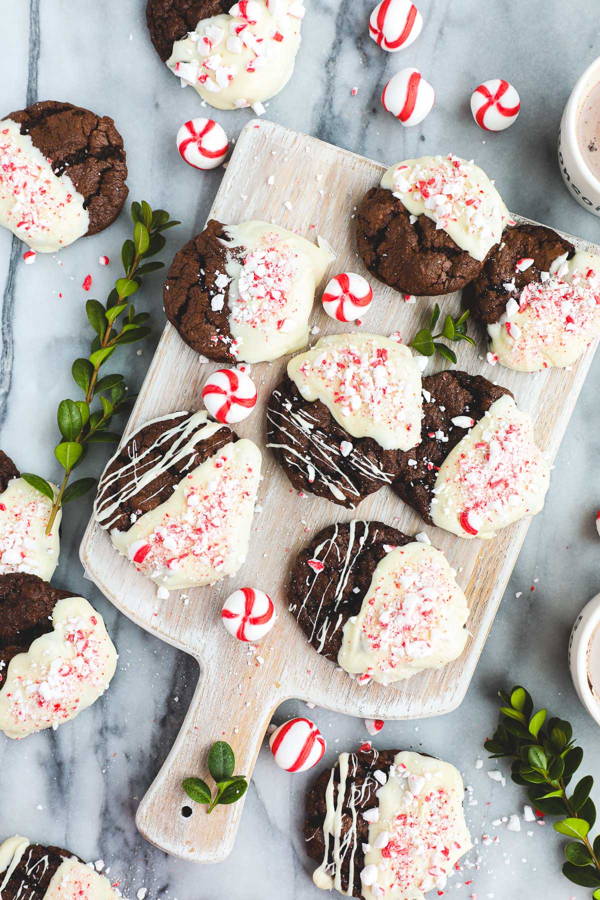 Peppermint Cocoa Cookies, chocolate cookies dipped in white chocolate with red and white crushed peppermint on top arranged on a white board.