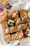 Blueberry Lemon Crumb Cake with Lemon Glaze drizzled on top, cut into squares on parchment paper.