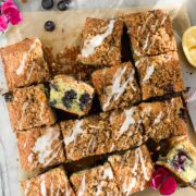 Blueberry Lemon Crumb Cake with Lemon Glaze drizzled on top, cut into squares on parchment paper.