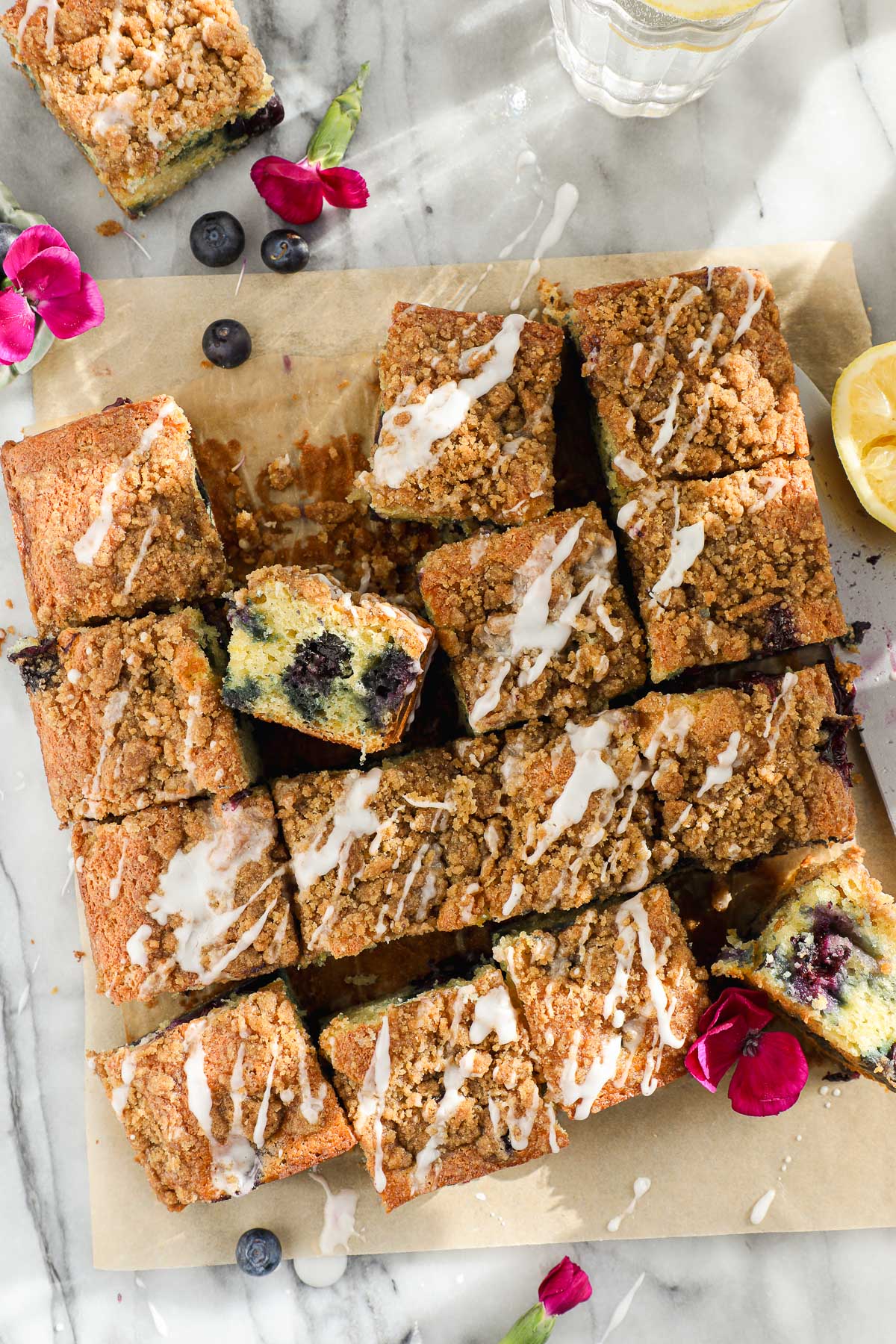 Blueberry Lemon Crumb Cake with Lemon Glaze drizzled on top, cut into squares on parchment paper.