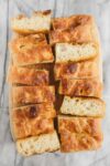 A loaf of golden Bubbly Focaccia cut into many pieces, some turned on their sides to show the bubbly interior.