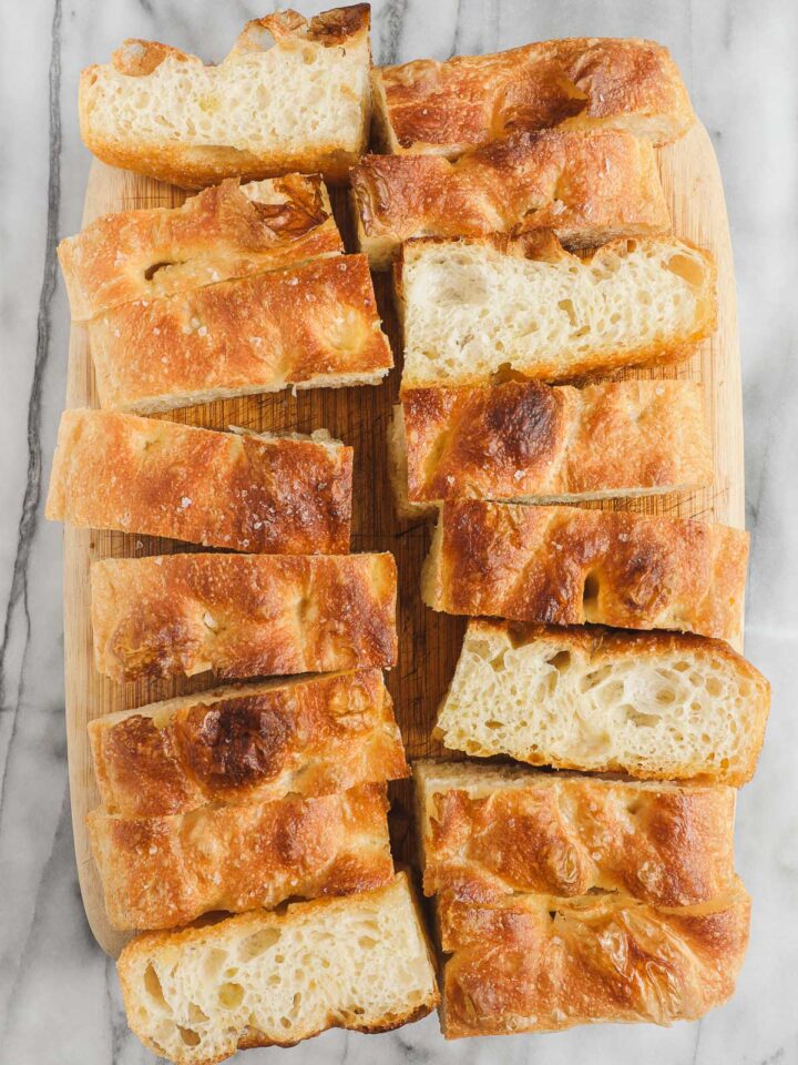 A loaf of golden Bubbly Focaccia cut into many pieces, some turned on their sides to show the bubbly interior.