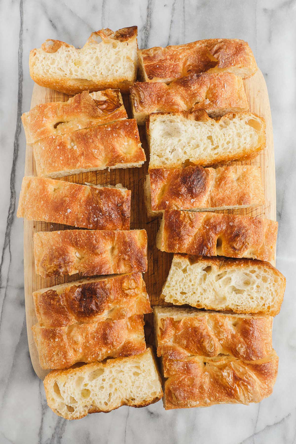 A loaf of golden Bubbly Focaccia cut into many pieces, some turned on their sides to show the bubbly interior.