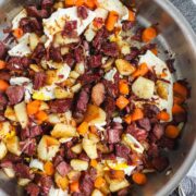 Corned Beef Hash in a large sauté pan with crispy corned beef, crispy potatoes, carrots, and pan fried eggs.