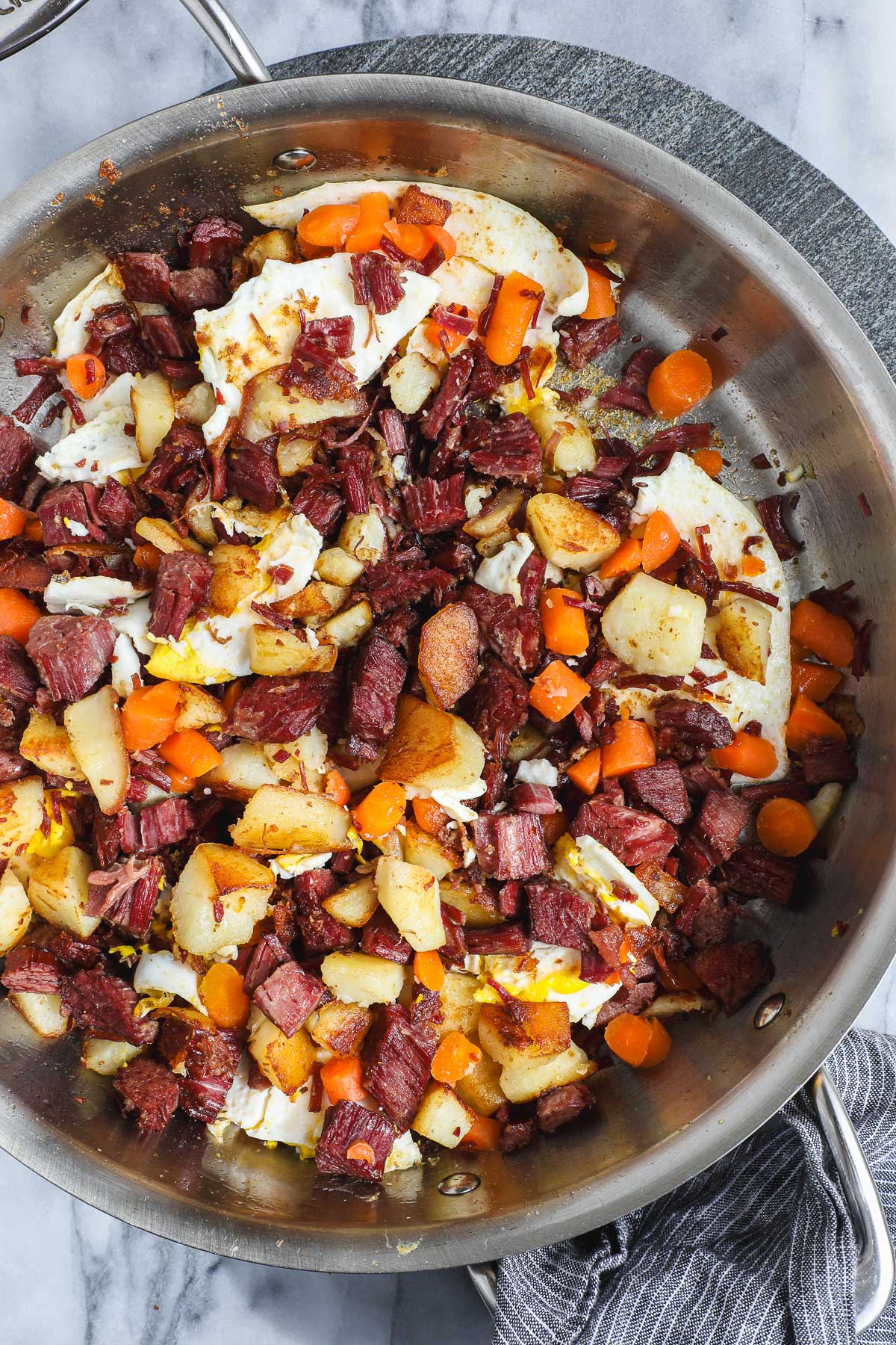 Corned Beef Hash in a large sauté pan with crispy corned beef, crispy potatoes, carrots, and pan fried eggs.