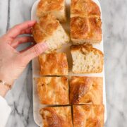 Loaf Pan Focaccia cut up into pieces and placed on a marble board with one piece turned on the side and Lauren picking up and holding another piece.
