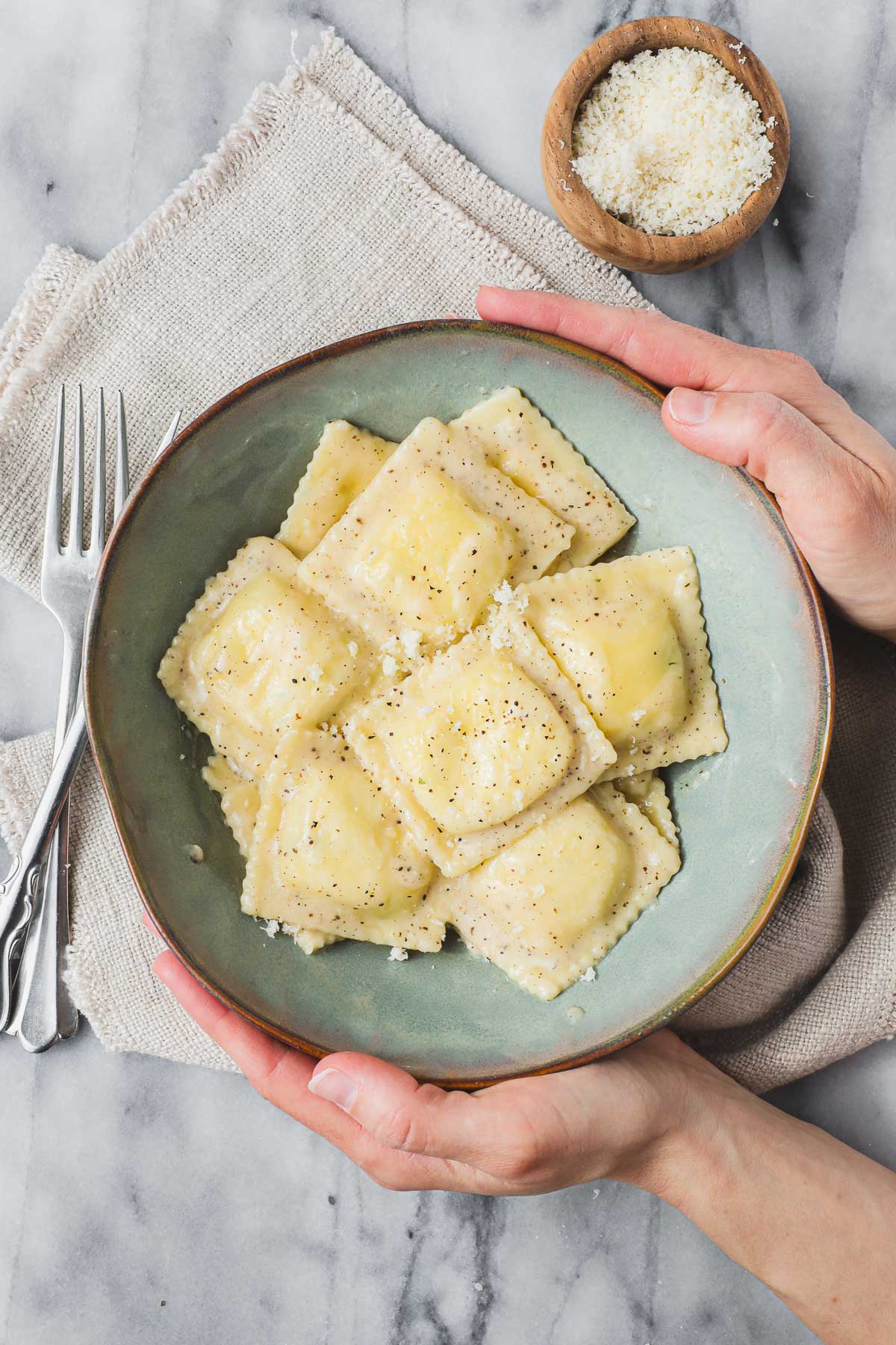 A blue green bowl with Ravioli Cacio e Pepe being held by Lauren on light background.