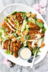 Caesar Salad with Crispy Chicken arranged on a white platter with romaine lettuce tossed with caesar dressing and sliced crispy chicken breast.