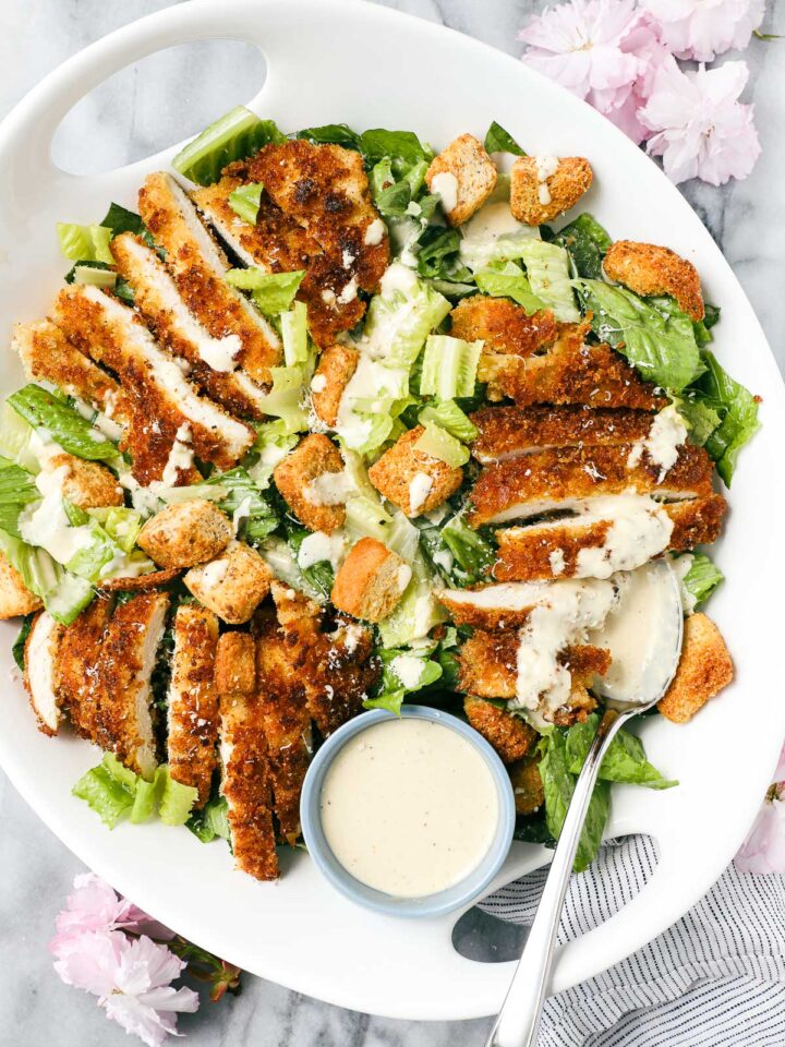 Caesar Salad with Crispy Chicken arranged on a white platter with romaine lettuce tossed with caesar dressing and sliced crispy chicken breast.