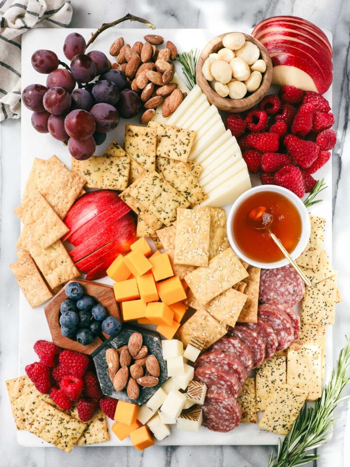Einkorn crackers on a charcuterie board surrounded by cheese, fruit, salami, and honey.
