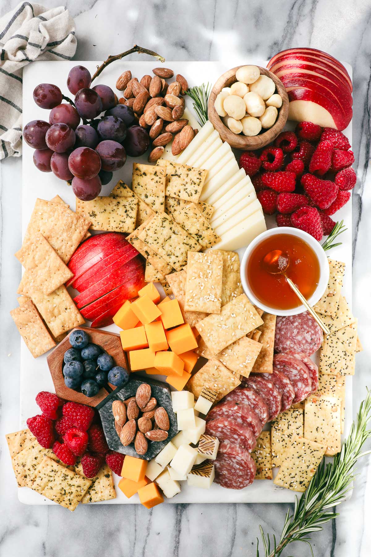 Einkorn crackers on a charcuterie board surrounded by cheese, fruit, nuts, salami, and honey.