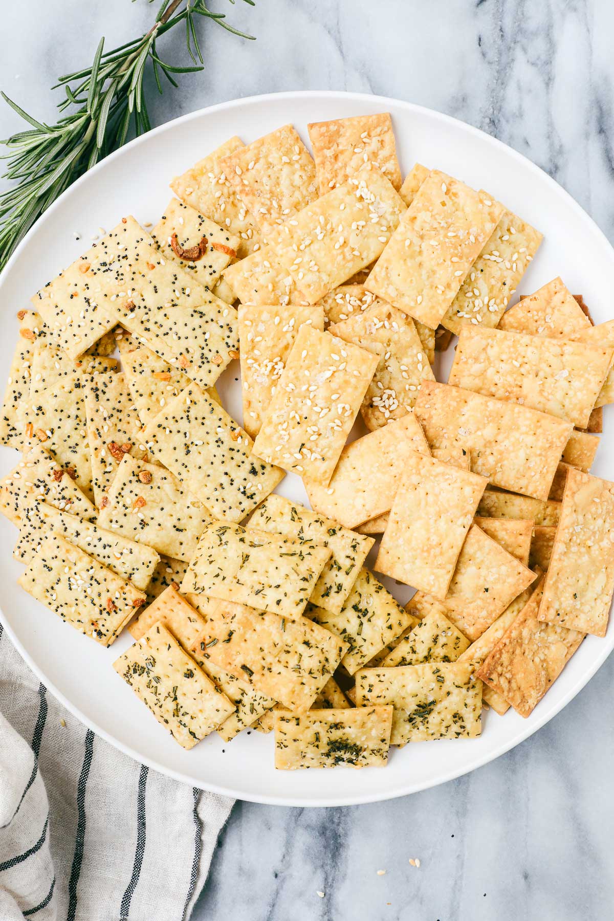 A plate with an array of sesame seed, flaky sea salt, rosemary, and everything bagel Einkorn crackers.