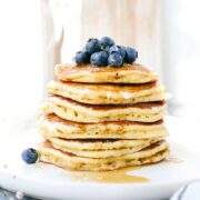 A stack of fluffy Einkorn pancakes on a plate topped with blueberries, butter, and maple syrup.