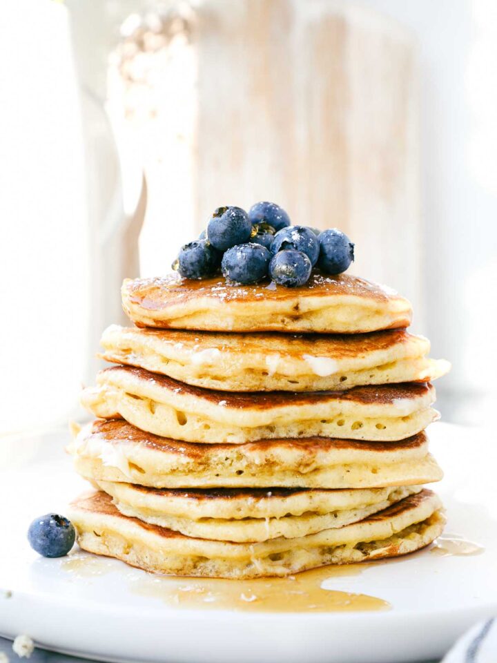 A stack of fluffy Einkorn pancakes on a plate topped with blueberries, butter, and maple syrup.