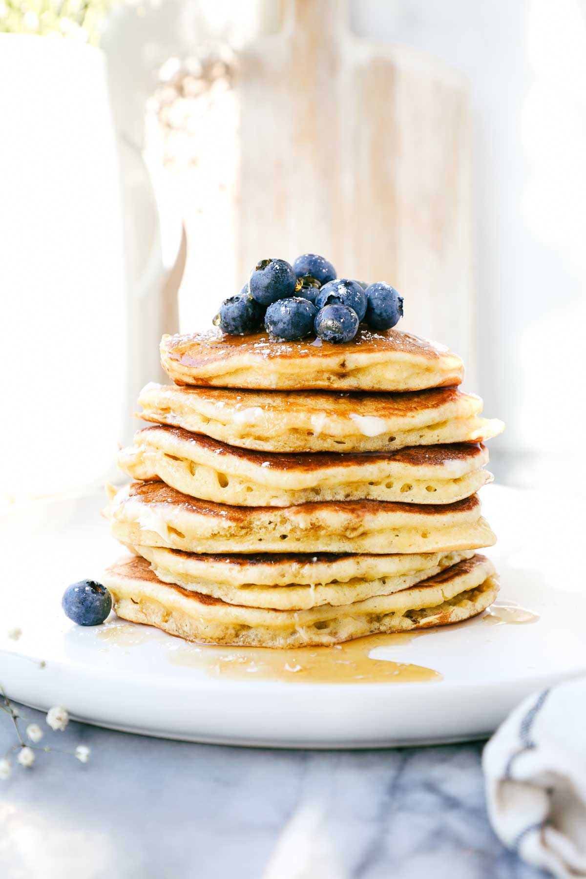A stack of fluffy Einkorn pancakes on a plate topped with blueberries, butter, and maple syrup.