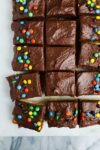 A 9x13 yellow cake made without a mixer with chocolate frosting decorated with M&Ms cut into square pieces.