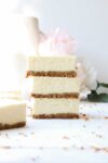 Three rectangular slices of cheesecake with a graham cracker crust stacked on top of each other with a light background.