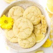 Lemon Olive Oil Cookies arranged on a plate on a white background decorated with yellow accents, lemons, and flowers.