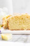 The cross section of a Lemon Olive Oil Loaf Cake showing the most and tender cake topped with a simple sweet lemon glaze on a light background.